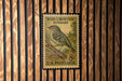A vintage 8-cent U.S. postage stamp featuring a bird perched on a branch, mounted on a wooden wall.