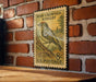 A vintage postage stamp featuring a bird, specifically a Ruby-Crowned Kinglet, is displayed on a brick wall.