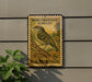 A postage stamp featuring a bird, specifically a Ruby-Crowned Kinglet, is mounted on a wall.