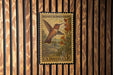 A vintage U.S. postage stamp featuring a hummingbird is displayed on a wooden wall.