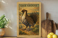 a framed illustration of a bird, specifically a Sage grouse, standing on a grassy field. The bird is depicted in a detailed and realistic manner, with its feathers and wings clearly visible. The framed artwork is placed on a shelf, surrounded by various kitchen utensils and items, such as a wooden cutting board and a potted plant.