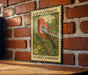 A vintage postage stamp featuring a red bird, likely a scarlet tanager, perched on a branch against a brick wall.