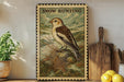 A vintage-style metal sign with a bird illustration, placed on a wooden shelf next to a potted plant and kitchen utensils.