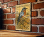 A vintage-style postage stamp featuring a bluebird perched on a branch, mounted on a brick wall.