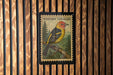 A postage stamp featuring a colorful bird, likely a Western Tanager, perched on a branch against a wood-paneled background.
