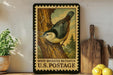 A framed vintage postage stamp depicting a white-breasted nuthatcher, a type of bird, is displayed on a shelf next to a wooden cutting board and some lemons.