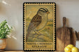 A framed illustration of a white-crowned sparrow is displayed on a shelf, accompanied by a wooden cutting board, a potted plant, and some lemons.