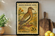 A vintage-style postage stamp depicting a white-winged dove, with a potted plant and wooden cutting board in the background.