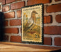 A vintage-style postage stamp depicting a white-winged dove, mounted on a brick wall.