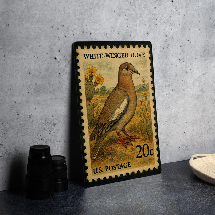 A vintage 20-cent U.S. postage stamp featuring a white-winged dove, placed on a gray countertop next to some black camera lenses.