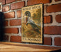 A vintage-style postage stamp featuring a wood duck on a brick wall.