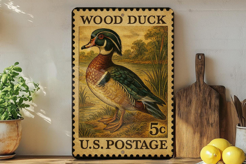 A vintage-style stamp depicting a wood duck, with the text "WOOD DUCK" and "U.S. POSTAGE" printed on it. The stamp is placed on a shelf next to a wooden cutting board and some potted plants.