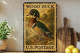 A vintage-style stamp depicting a wood duck, with the text "WOOD DUCK" and "U.S. POSTAGE" printed on it. The stamp is placed on a shelf next to a wooden cutting board and some potted plants.