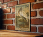 A vintage 25c U.S. postage stamp featuring a wood stork illustration is displayed on a wooden surface against a brick wall.