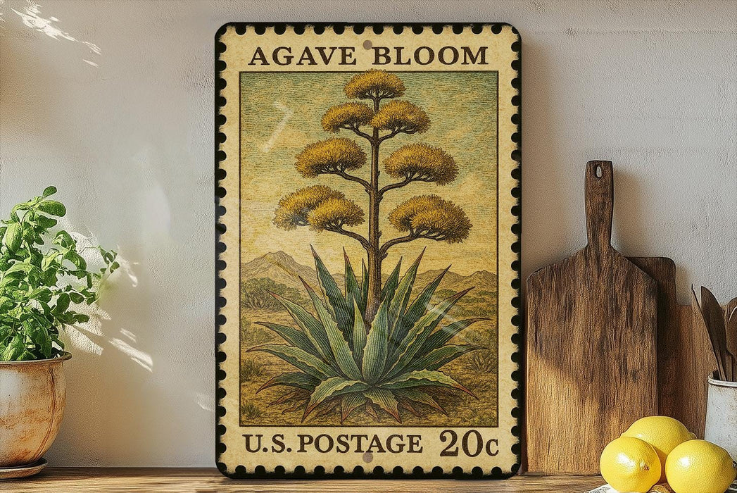 A framed postage stamp depicting an agave plant, with the text "AGAVE BLOOM" and "U.S. POSTAGE 20¢" printed on it. The stamp is placed on a shelf next to a wooden cutting board and a potted plant.