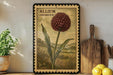 a framed illustration of a red flower, possibly an allium, on a shelf next to a wooden cutting board and some kitchen utensils.