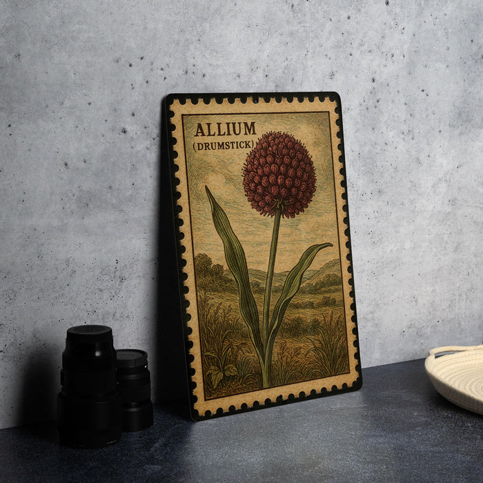 A framed illustration of a red flower, resembling a tulip, is displayed on a table next to a stack of black camera lenses.