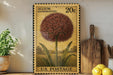A vintage-style postage stamp featuring a large flower illustration, placed on a wooden surface next to a wooden cutting board and a potted plant.