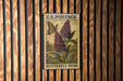 A U.S. postage stamp featuring a butterfly and a flowering bush, mounted on a wooden wall.