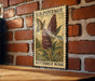 A vintage U.S. postage stamp featuring a butterfly and a flowering bush, mounted on a brick wall.