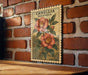 A vintage-style postage stamp featuring a floral illustration of two red flowers against a brick wall background.