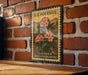 A vintage-style U.S. postage stamp featuring a floral design, mounted on a brick wall.