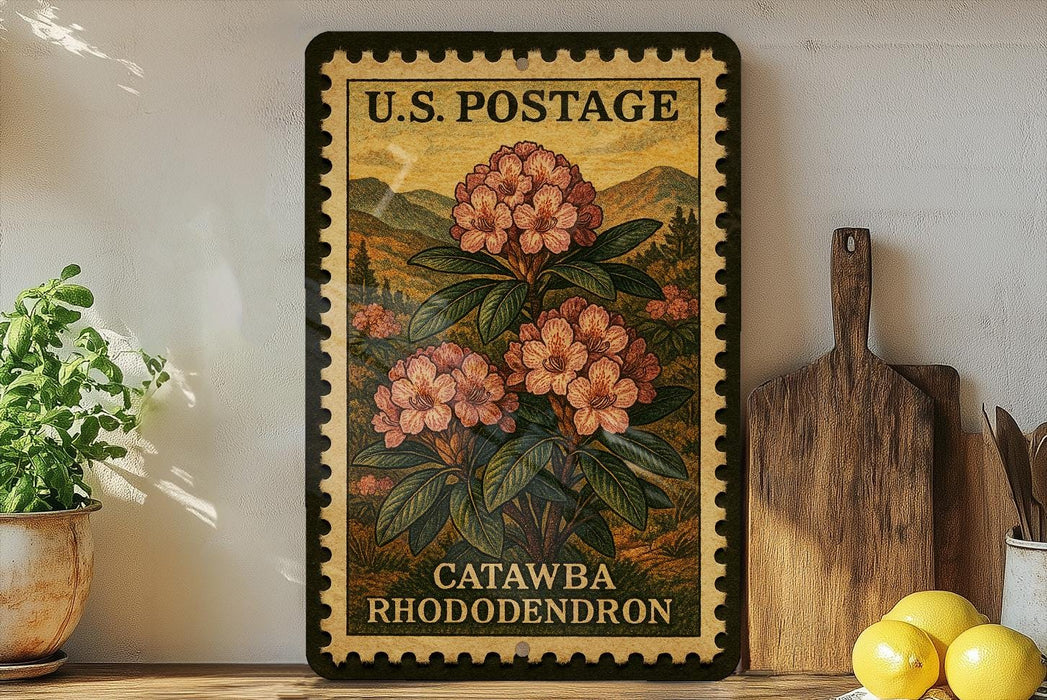 A framed vintage U.S. postage stamp depicting a large pink flower, with the text "U.S. POSTAGE" and "CATAWBA RHODODENDRON" printed on it. The stamp is displayed on a shelf next to a wooden cutting board and a potted plant.