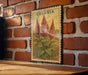 A vintage celosia plant stamp is displayed on a brick wall, with a wooden table below it.