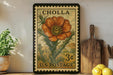 A vintage postage stamp featuring a large orange flower is displayed on a shelf, surrounded by kitchen utensils and a potted plant.