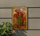 A U.S. postage stamp featuring a cactus plant with red flowers, mounted on a wall next to a plant.