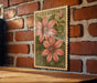 A framed illustration of clematis flowers is displayed on a brick wall, with a wooden table below it.