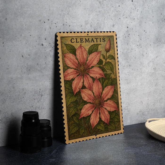 A framed botanical illustration of clematis flowers is displayed on a gray wall, accompanied by a stack of black camera lenses and a white dish.