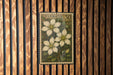 A framed print of a Clematis flower is hanging on a wooden wall.