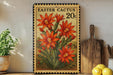 A framed stamp depicting a vibrant red cactus flower, with the text "EASTER CACTUS 20c" printed on it. The stamp is placed on a wooden shelf, surrounded by various kitchen utensils and a potted plant.