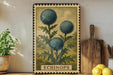 a framed illustration of three blue flowers with green leaves, placed on a shelf next to a wooden cutting board and a potted plant.