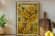 a framed stamp with a floral design, placed on a shelf next to a wooden cutting board and some potted plants.