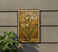 A wooden postage stamp featuring an illustration of two white orchid flowers, with the text "USA 20c" and "Fringed Orchid" printed on it. The stamp is mounted on a wall, and there is a plant visible to the left of the stamp.