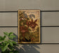 a wooden postcard with a floral illustration, hanging on a wall next to a plant.