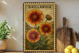 a framed illustration of three large sunflowers, with the word "GAILLARDIA" written above them. The frame is placed on a wooden surface, with a potted plant to the left and a wooden cutting board to the right. There are also some lemons visible in the image.