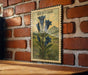 A framed illustration of blue bell-shaped flowers is hanging on a brick wall.