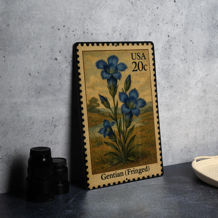 A postage stamp featuring a blue iris flower, with the text "USA 20c" and "Gentian (Fringed)" printed on it. The stamp is placed on a table next to some black camera lenses.