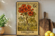 A vintage-style postage stamp featuring a vibrant illustration of a geranium plant, with the word "GERANIUM" printed below the floral design. The stamp is displayed on a shelf next to a wooden cutting board and a potted plant, creating a rustic and charming scene.