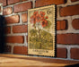 A vintage-style postage stamp featuring a vibrant illustration of a geranium plant, mounted on a brick wall.