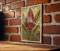 a framed illustration of a red flower on a brick wall.