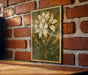 a framed painting of a white flower on a brick wall.