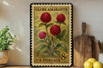 A vintage-style postage stamp featuring a vibrant illustration of red flowers, placed on a wooden surface next to a wooden cutting board and a potted plant.