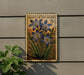 A wooden sign with a floral design hangs on a wall, featuring a large blue flower surrounded by green leaves.