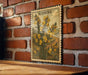 A framed illustration of a plant with yellow flowers is displayed on a brick wall.