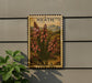 A framed image of a plant with red flowers is mounted on a wall, next to a small green plant.