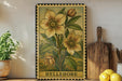 A framed illustration of a flower is displayed on a shelf, accompanied by a wooden cutting board, a potted plant, and some lemons.